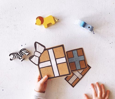 Eine Kinderhand hält kleine Geschenke, daneben sind Holztiere zu sehen. 
