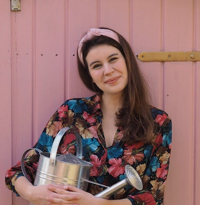 Anna vor ihren Gartenhäusschen, sie umarmt eine Gieskanne